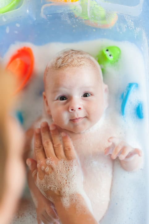 Mother bathing baby in tub with water and bubbles lather