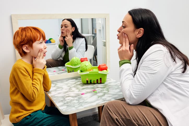 Speech therapy. Therapist shaping a boy’s mouth in order for his to make correct sound