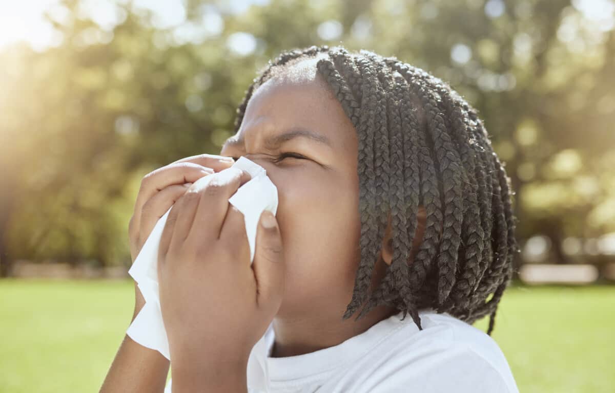 Covid, health and black kid blowing nose at park, nature or outdoors. Wellness, healthcare and sick girl child with tissue to wipe nose for virus, infection or cold, flu or covid 19, fever or allergy