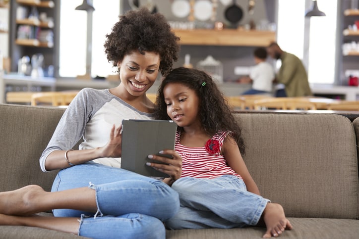 Mother And Daughter Sit On Sofa In Lounge Using Digital Tablet