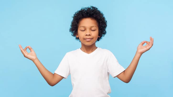 Portrait of peaceful cute little boy holding fingers in mudra gesture and meditating with closed eyes, feeling calm positive