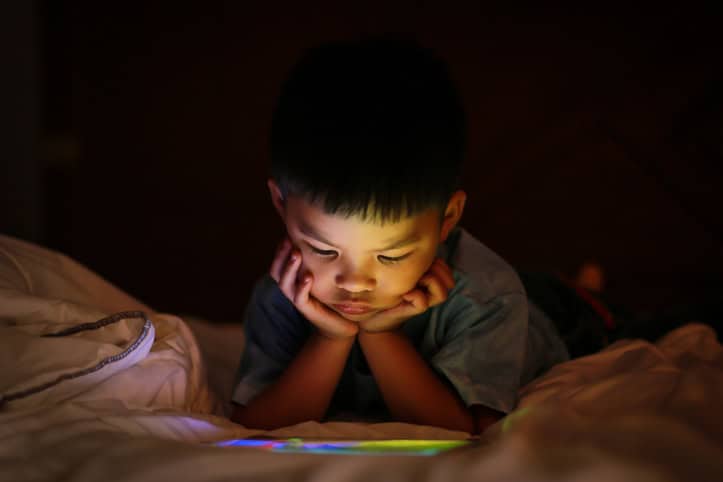 Asian boy watching colorful bright tablet screen in dark.